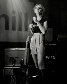 a woman standing in front of a microphone on top of a stage with a guitar