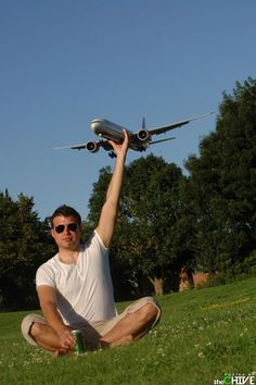 a man sitting in the grass holding up a model airplane