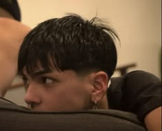 a young man with black hair and piercings on his ears looking off into the distance