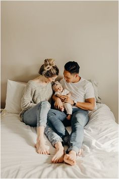 a man and woman sitting on top of a bed with their baby in their arms