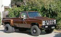 a large brown truck parked on the side of a road next to bushes and trees