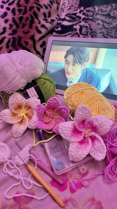 a laptop computer sitting on top of a bed covered in pink and purple yarn next to flowers