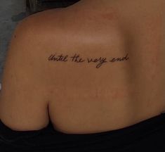 the back of a woman's shoulder with a tattoo that reads, until the very end