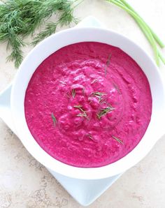 a white bowl filled with beet soup and topped with fresh dill sprigs