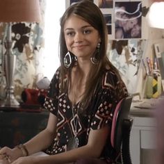 a woman sitting at a desk in front of a lamp and some pictures on the wall