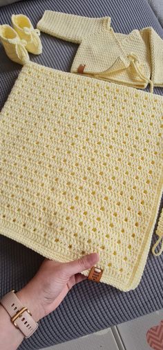 a crocheted blanket is being held up by a woman's hand on the floor