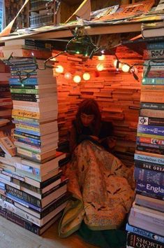 a woman sitting in a pile of books under a tent made out of stacked books