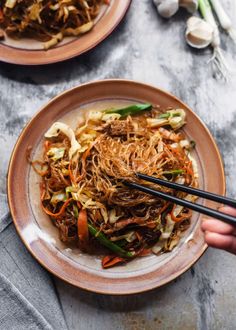 someone holding chopsticks over a plate of stir fried noodles with vegetables on the side