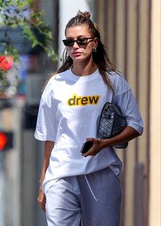 a woman walking down the street in sweatpants and a t - shirt with drew written on it