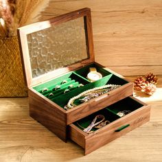 an open wooden box with jewelry in it on a table next to a pine cone