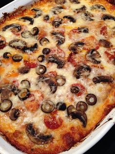 a pizza with cheese, mushrooms and sauce in a white casserole dish on a black surface