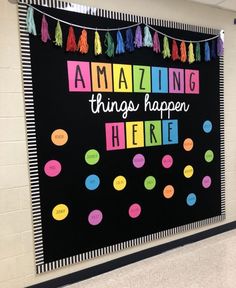 a bulletin board with the words amazing things happen here written in bright colors and tassels