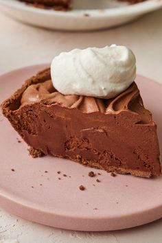 a slice of chocolate pie with whipped cream on top sits on a small pink plate