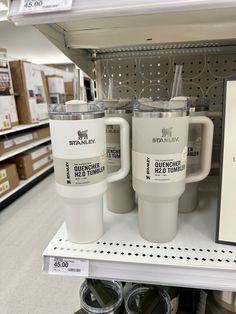 two white coffee mugs sitting on top of a shelf next to a black and white sign