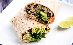 a burrito cut in half sitting on top of a white plate next to bowls of salad