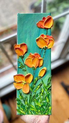 a person holding up a piece of art with flowers painted on it