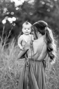 a woman holding a baby in her arms and looking at the sky with trees in the background