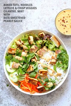 a white bowl filled with salad next to a cup of dressing on top of a table