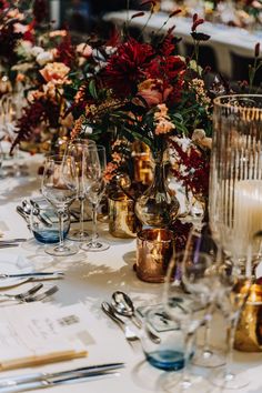 the table is set with silverware, wine glasses and flowers in gold vases