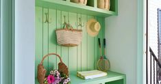 a green bench with baskets and flowers on it next to a wall mounted coat rack