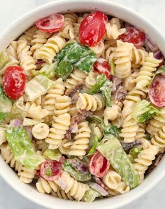 a pasta salad with tomatoes, lettuce and other vegetables in a white bowl