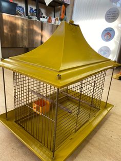 a yellow bird cage sitting on top of a wooden floor next to a metal shelf