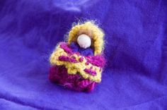 a knitted doll sitting on top of a purple cloth