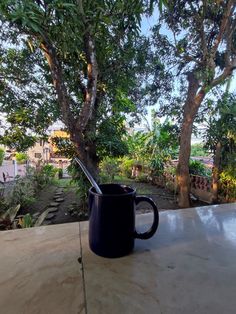 a black coffee mug sitting on top of a wooden table next to a green tree