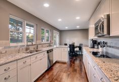 a large kitchen with white cabinets and marble counter tops, along with hardwood flooring