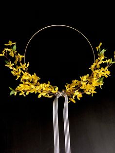 a wreath with yellow flowers and ribbons hanging from it's sides on a black background