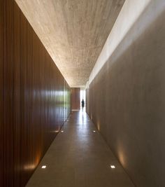 the hallway is lined with wooden panels and concrete walls, leading to an open area