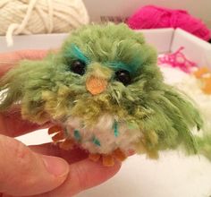 a small green bird with blue eyes sitting on top of a persons hand next to balls of yarn