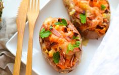 two stuffed potatoes on a white plate next to a fork