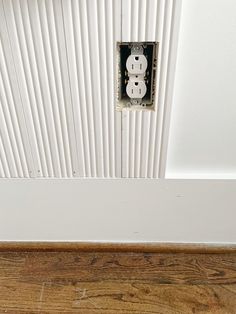 an electrical outlet on the side of a wall with wood flooring and white paint