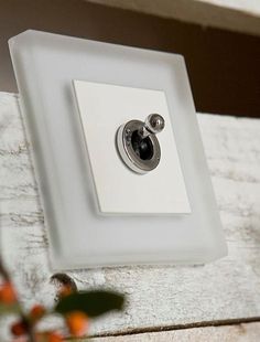 a white light switch sitting on top of a wooden table next to flowers and leaves