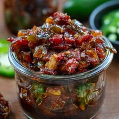 a glass jar filled with food sitting on top of a wooden table next to green peppers