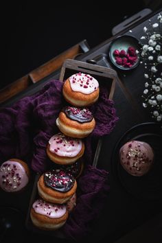 a box filled with lots of donuts on top of a purple cloth next to other desserts