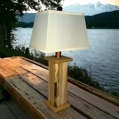 a lamp sitting on top of a wooden table next to a lake with mountains in the background