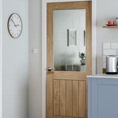 a kitchen with a clock on the wall and a wooden door in front of it