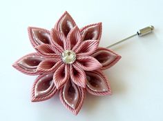 a pink flower brooch sitting on top of a white table next to a needle