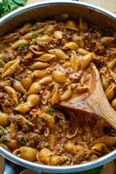 a pot filled with pasta and meat on top of a wooden table next to a spoon