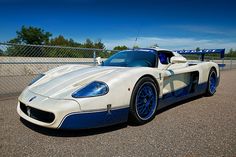 a white and blue sports car parked in a parking lot next to a chain link fence