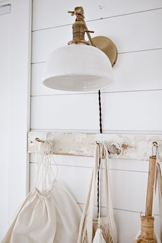 three bags hanging from hooks on the wall next to a lamp and other items in front of them