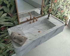 a marble sink in front of a mirror and wallpapered with tropical leaves on the walls