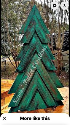 a green wooden christmas tree sitting on top of a wooden floor in front of trees