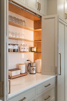 a kitchen with white cupboards and wooden shelves filled with glassware, tea kettle and coffee pot