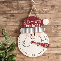 a clock with a santa hat on it hanging from a wooden wall next to a christmas tree