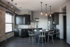 a kitchen with black cabinets and white counter tops, dark wood flooring and bar stools