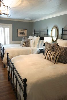 two beds in a room with wooden flooring and white bedding, one is made up