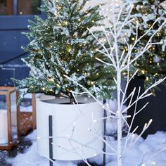 a small christmas tree in a white planter with snow on the ground next to it